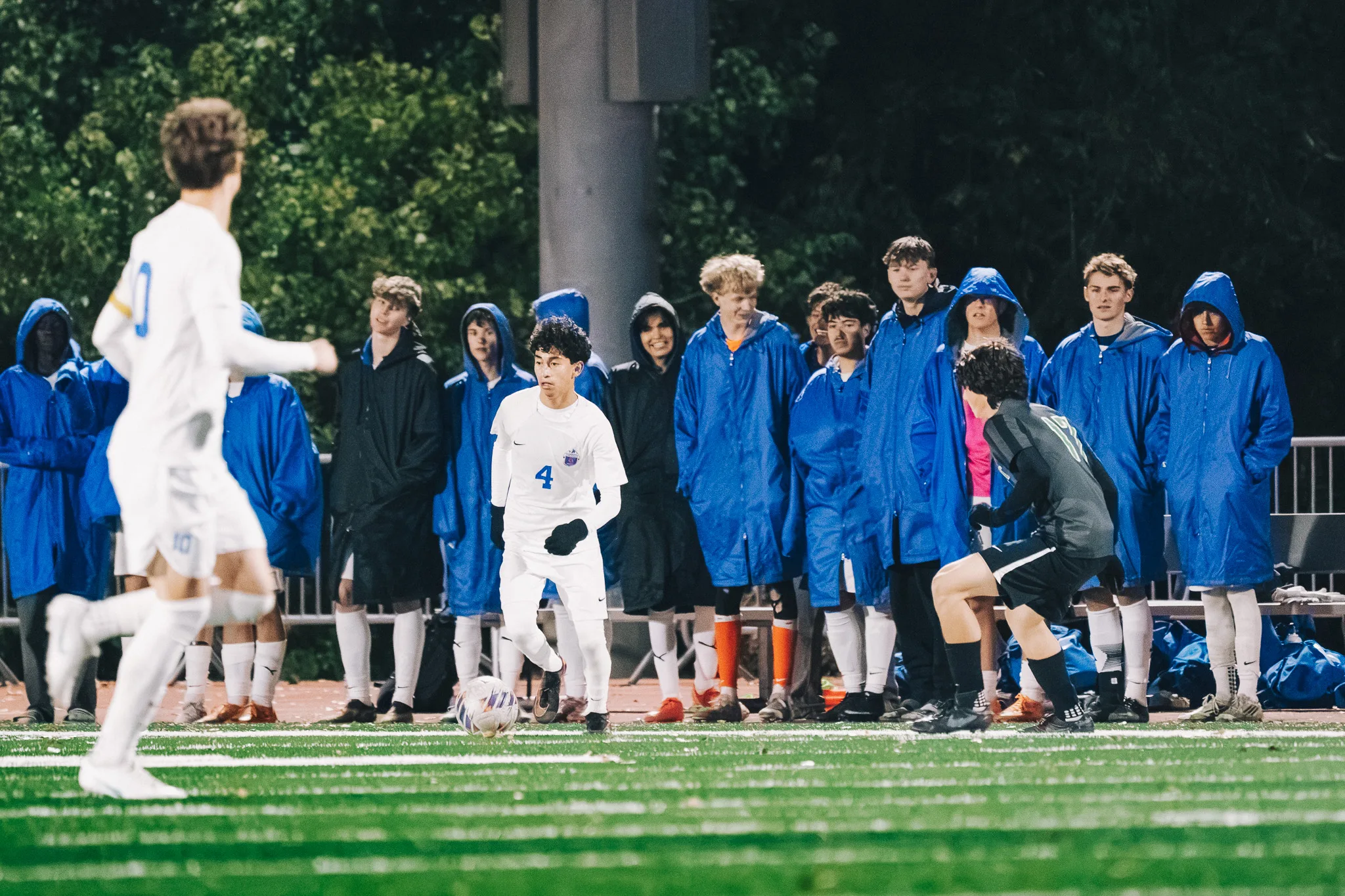 Centaurus number 4 dribbles toward a Niwot player in front of the Centaurus bench, teammates in blue parkas watching from the sideline