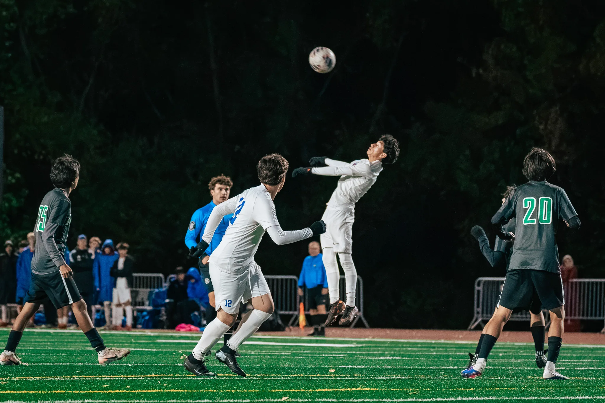A Centaurus player arches back with his arms out under a high ball as Centaurus number 12, Niwot numbers 25 and 20 and the referee in blue look on