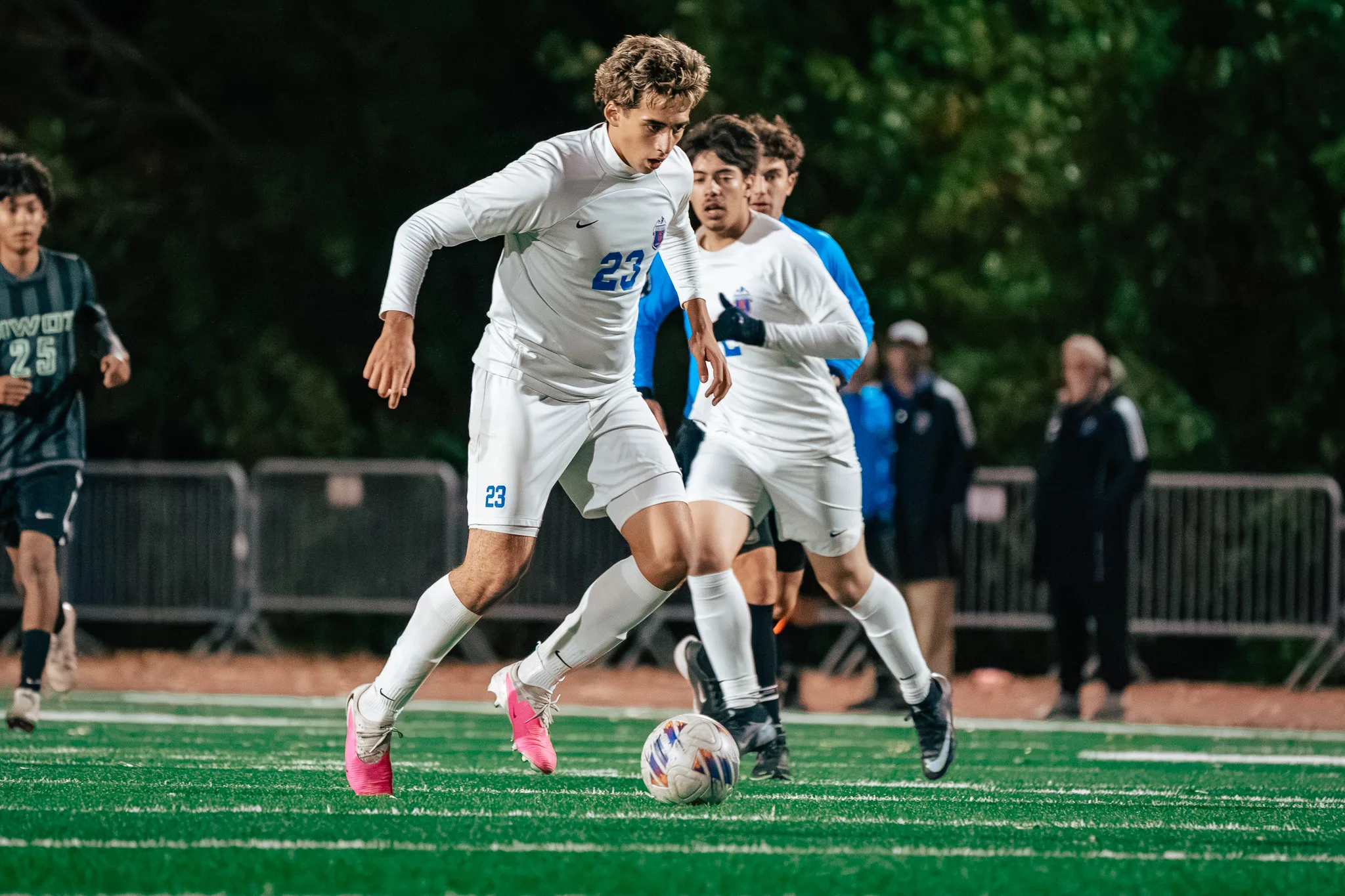 Centaurus number 23 in pink cleats dribbles forward, a teammate and the referee in blue behind him and Niwot number 25 at the left