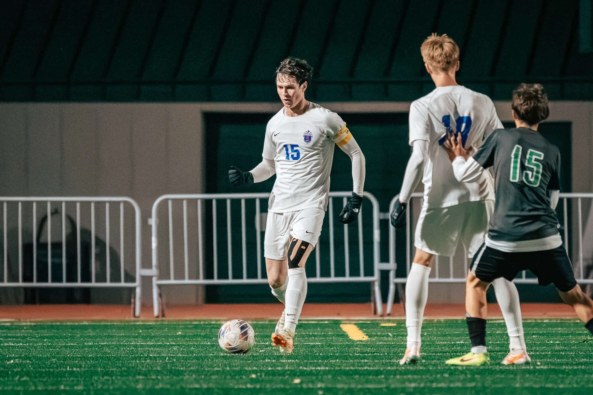Centaurus number 15 in a yellow armband brings the ball forward as Niwot number 15 leans on a Centaurus teammate at the right