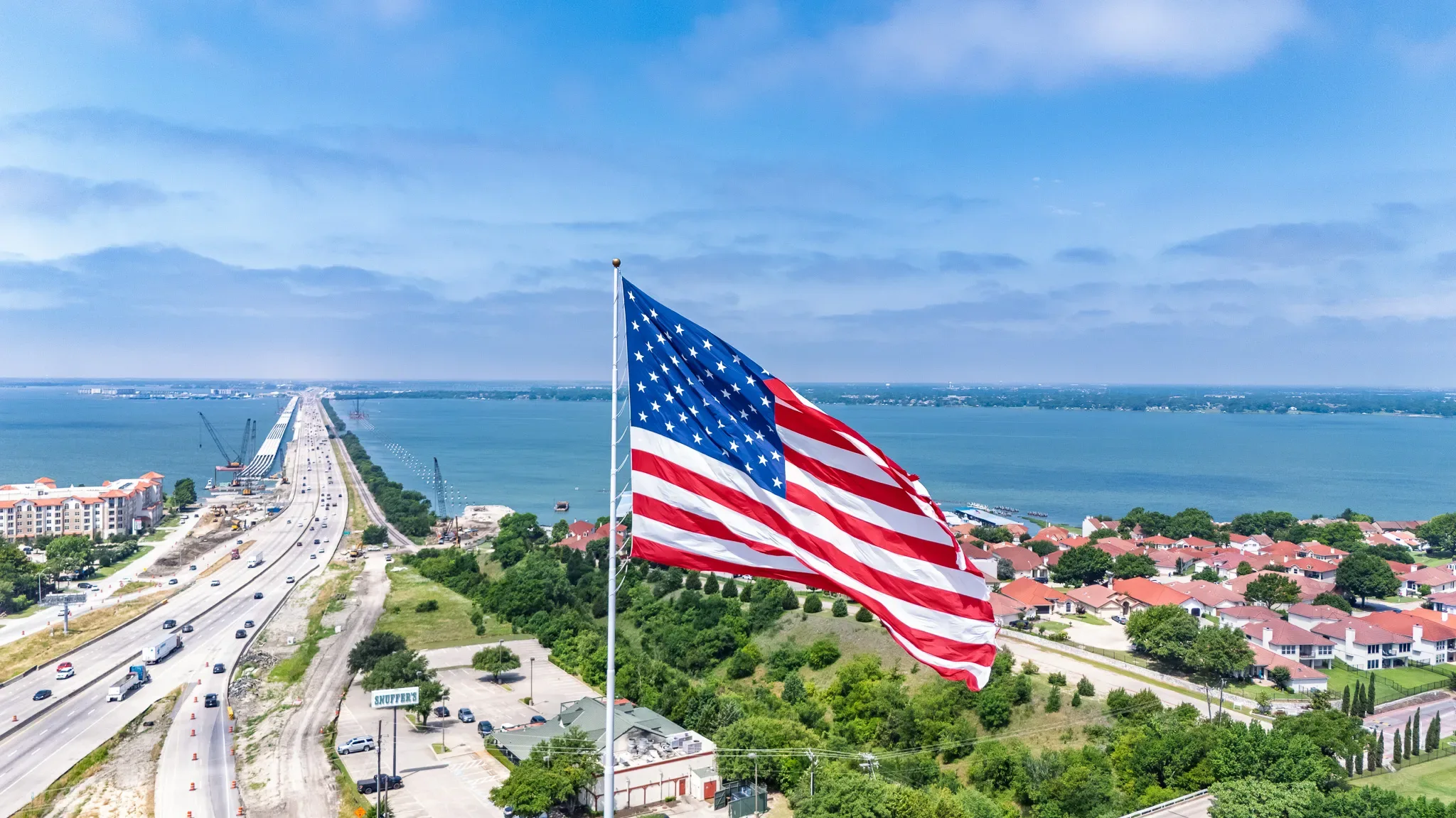 Giant American flag flying beside Interstate 30 in Rockwall, Texas, with Lake Ray Hubbard and the highway bridge beyond