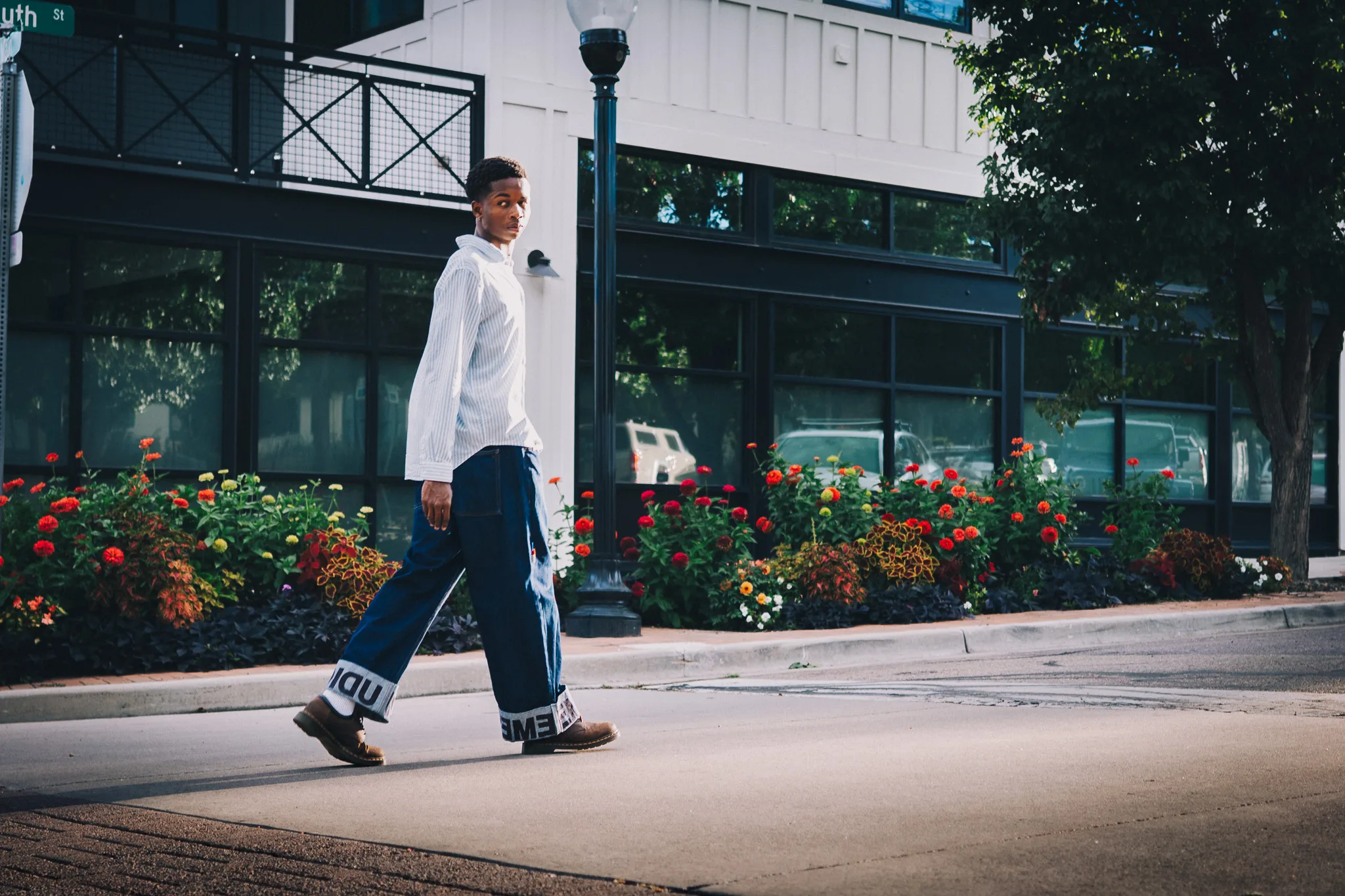 Charlie strides past a bed of red and orange flowers on a downtown sidewalk.
