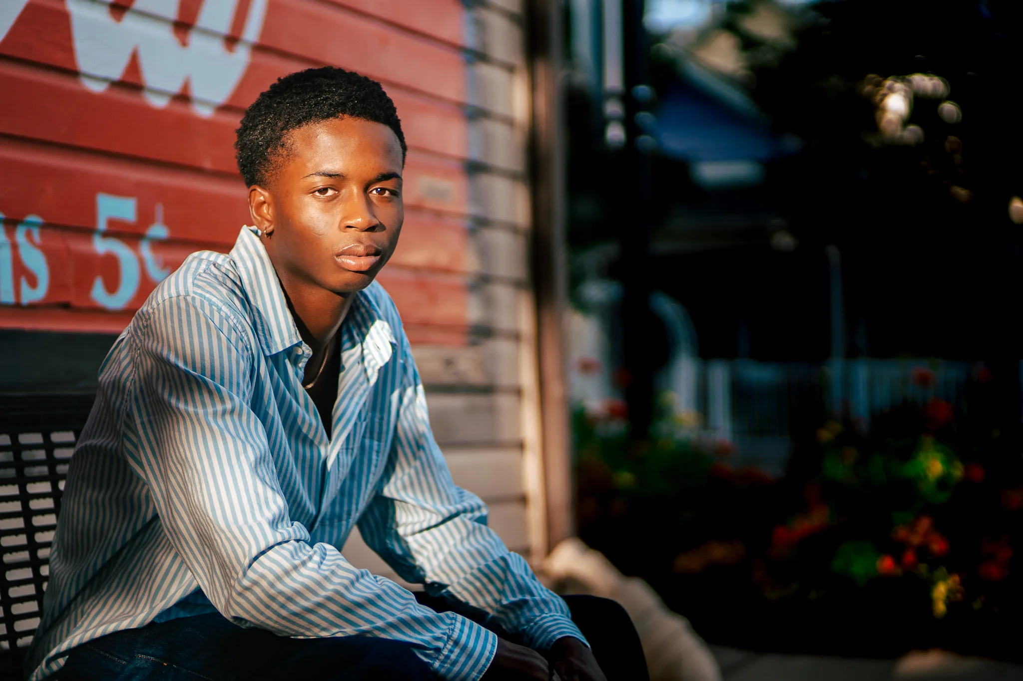 Charlie sits beside a red painted wall in warm evening light, wearing a blue striped shirt.