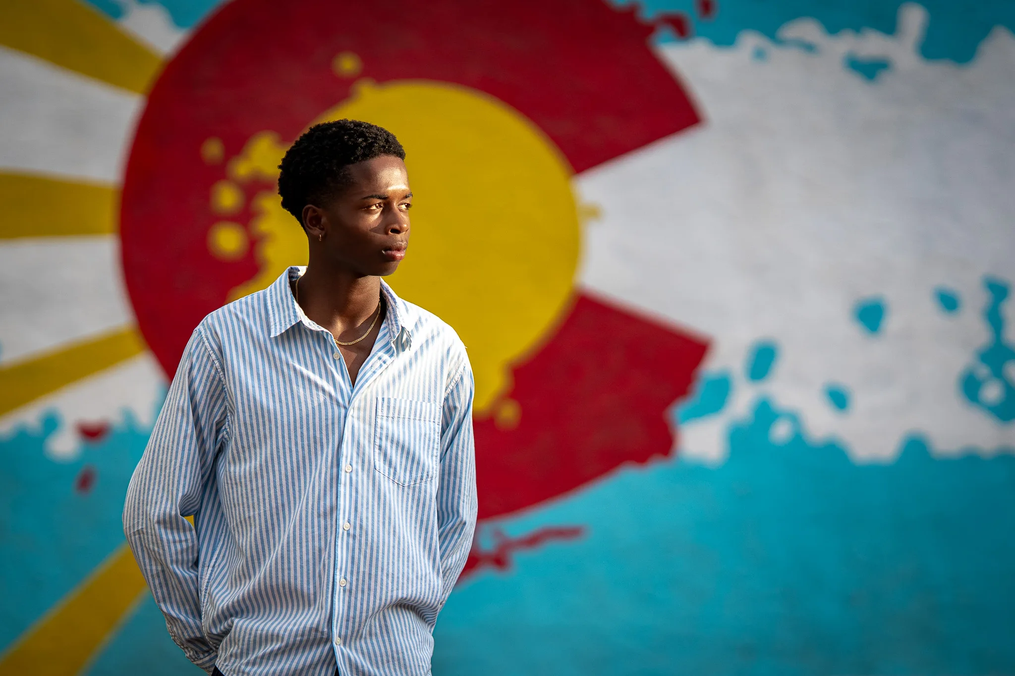 Charlie stands in front of a painted Colorado flag mural in downtown Louisville, looking off to the side.
