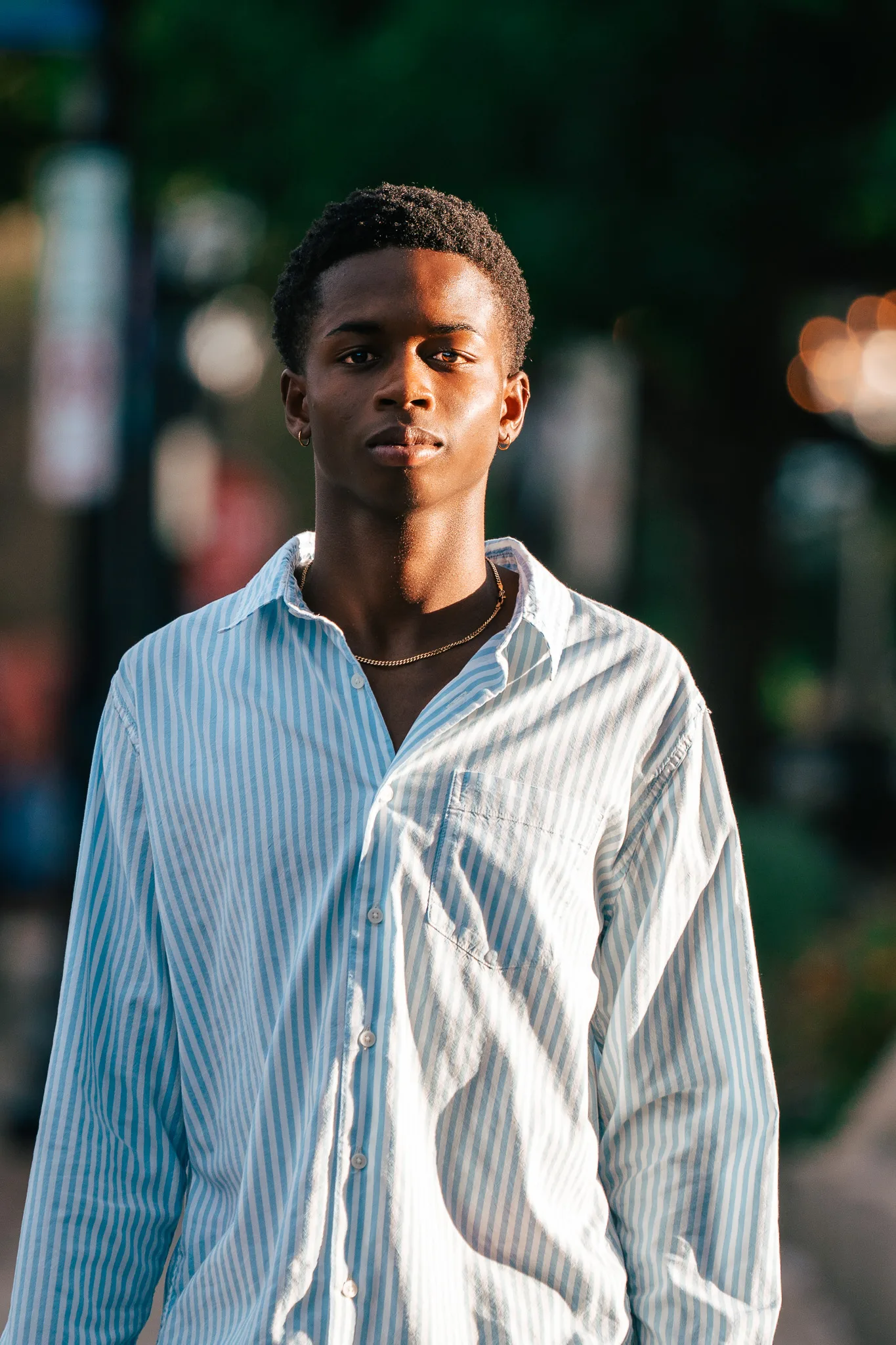 Charlie faces the camera in a loose blue striped shirt, the downtown street glowing behind him.