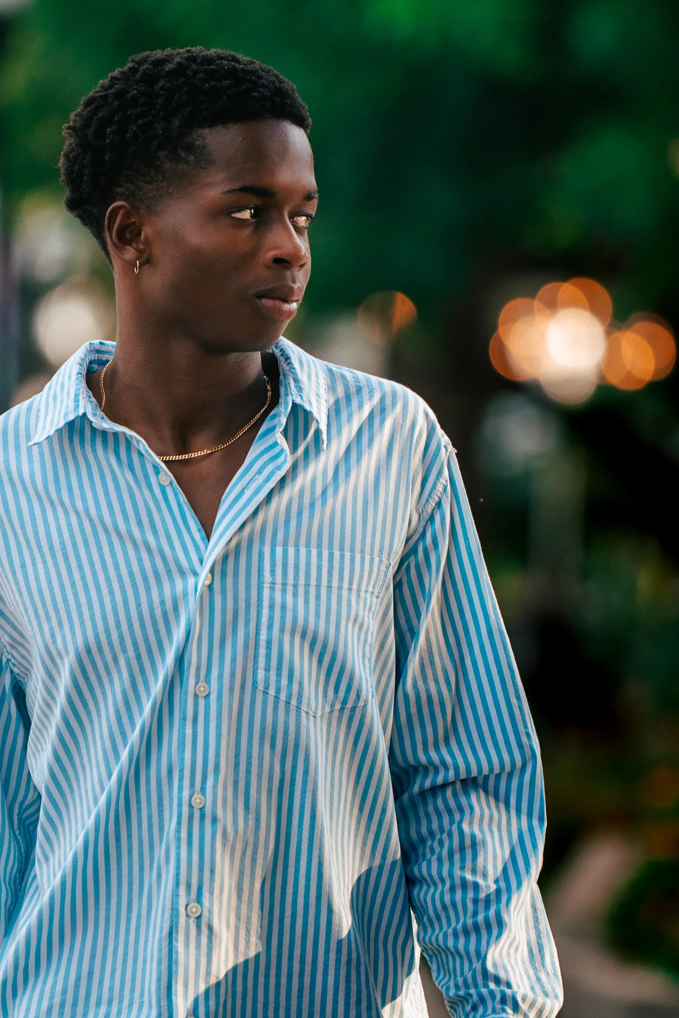 Charlie glances to the side in a blue striped shirt, warm street lights blurred behind him.