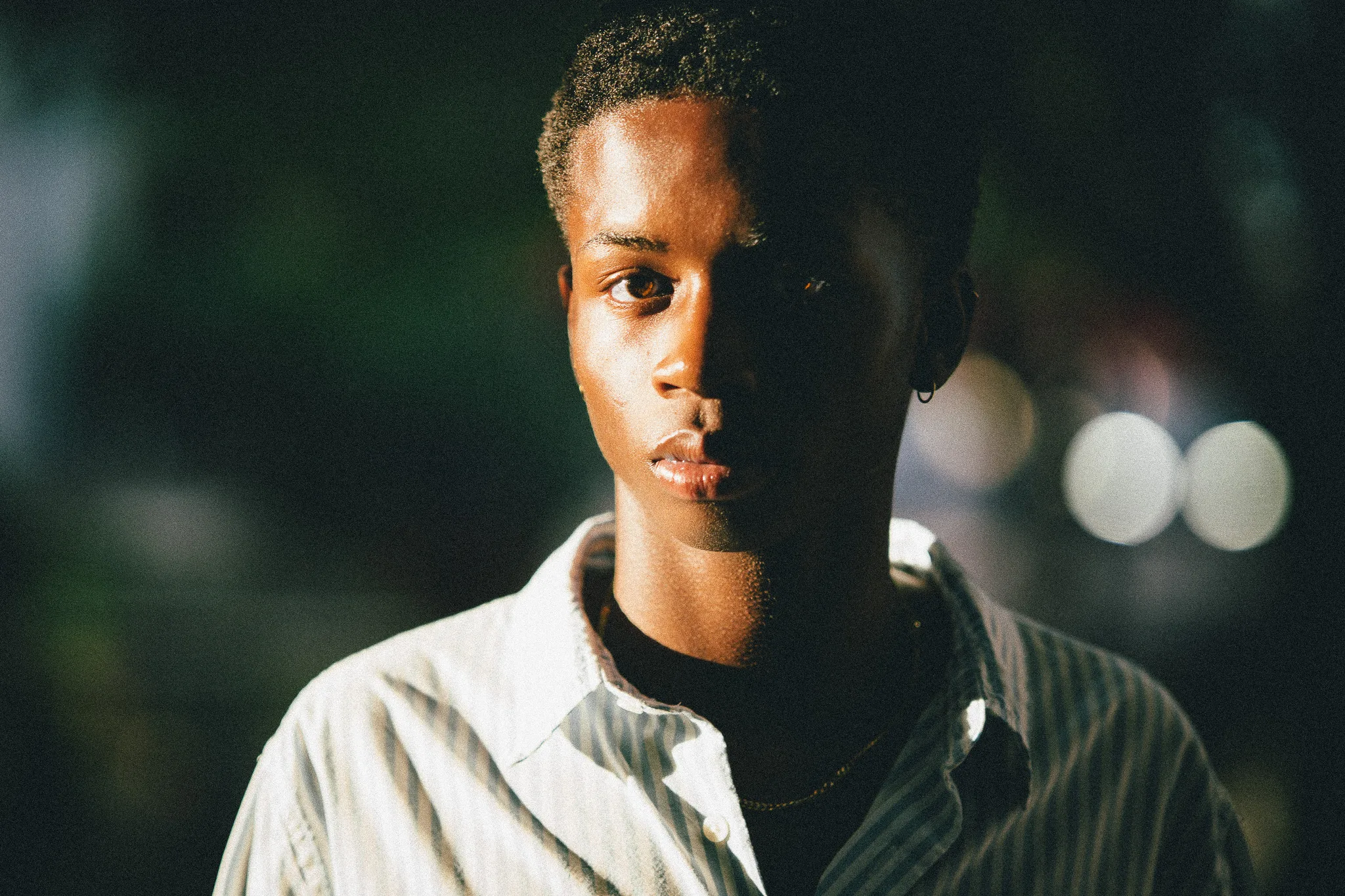 Close portrait of Charlie with half his face in shadow and bright bokeh behind him.