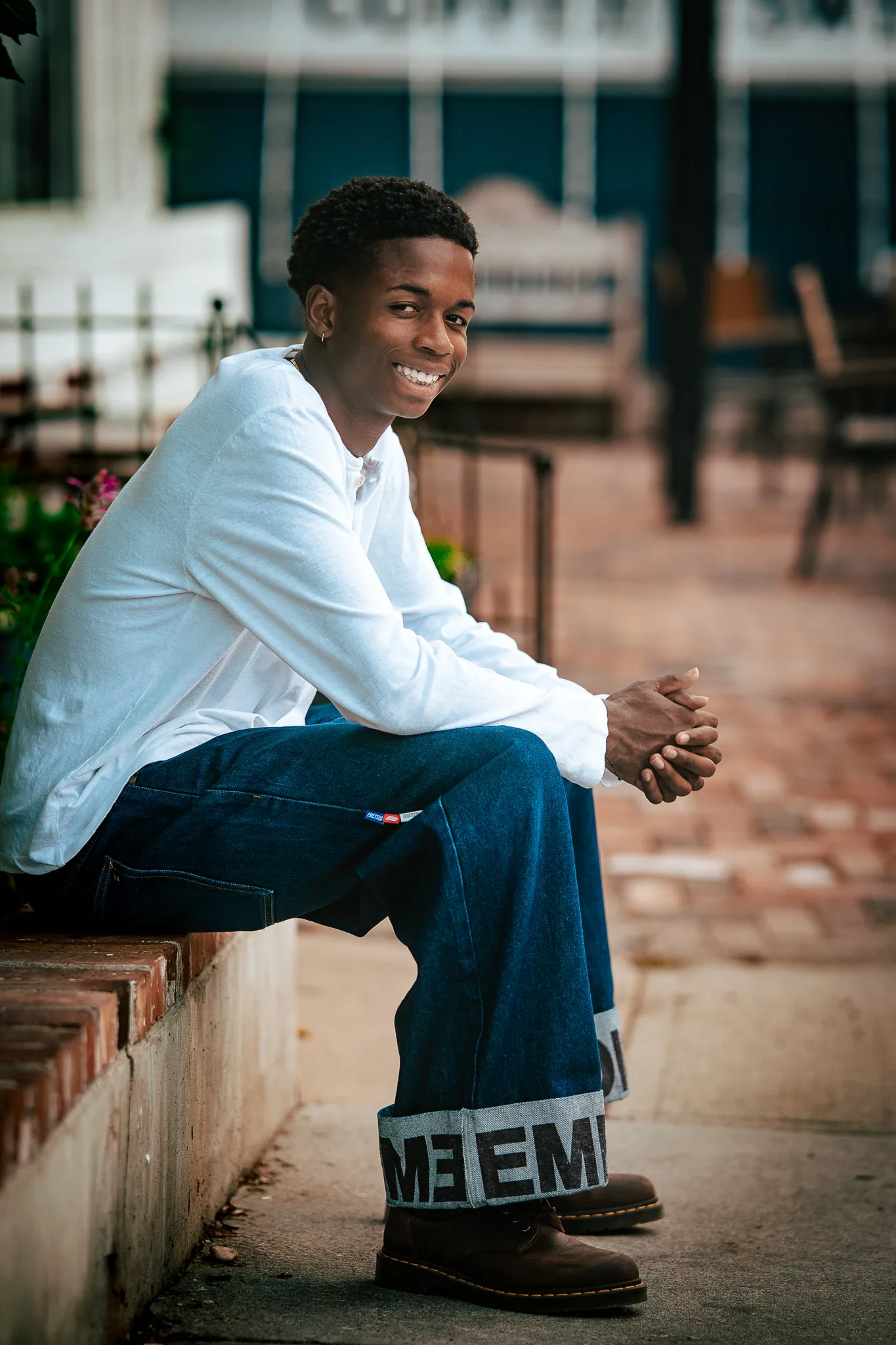 Charlie smiles from a brick ledge in a white henley and wide-leg jeans with printed cuffs.