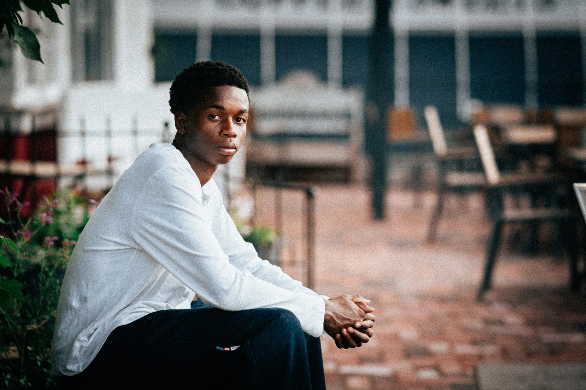 Charlie sits on a patio ledge in a white henley, hands clasped, looking at the camera.