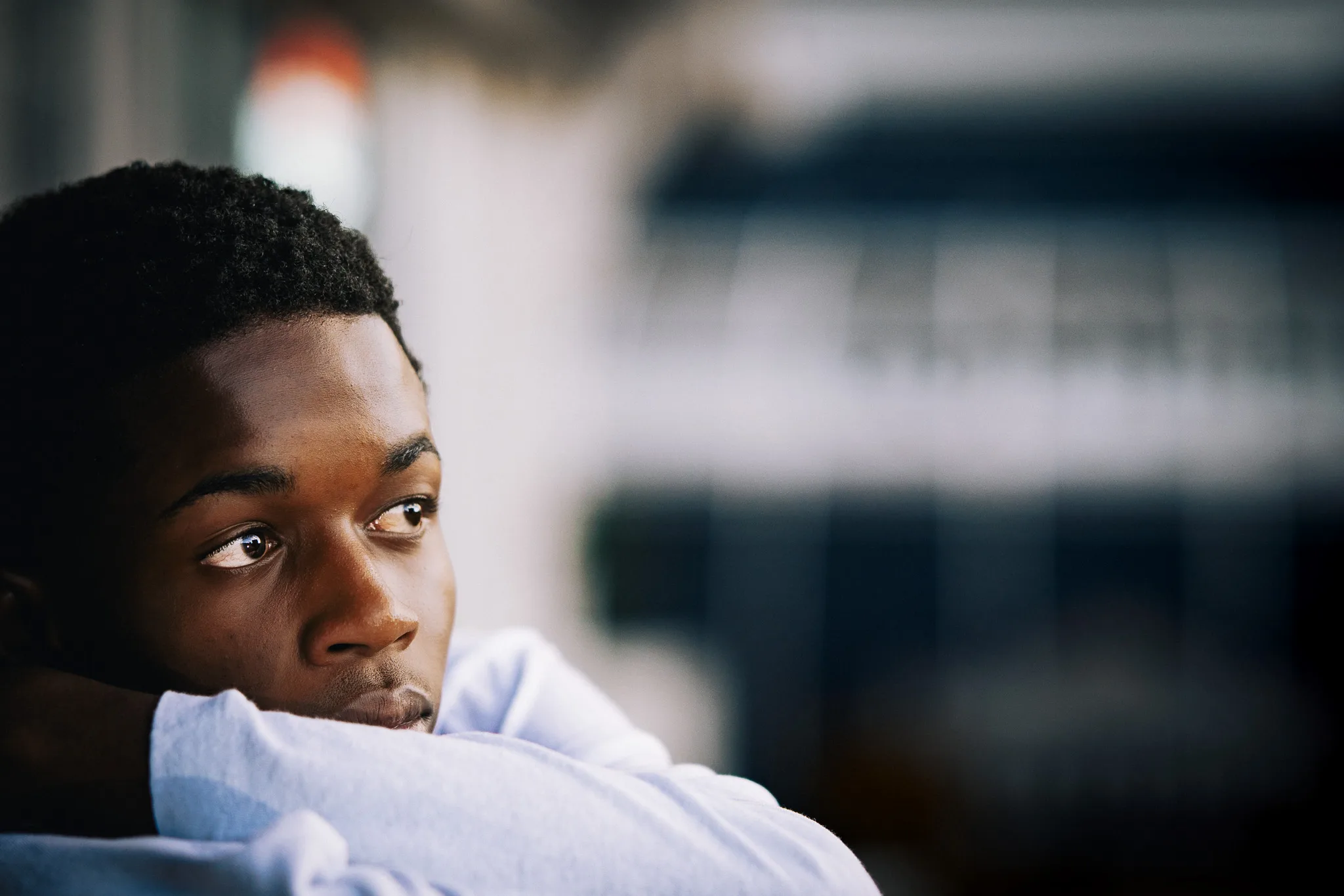 Charlie rests on his folded arms, gazing off to the side, a storefront blurred behind him.