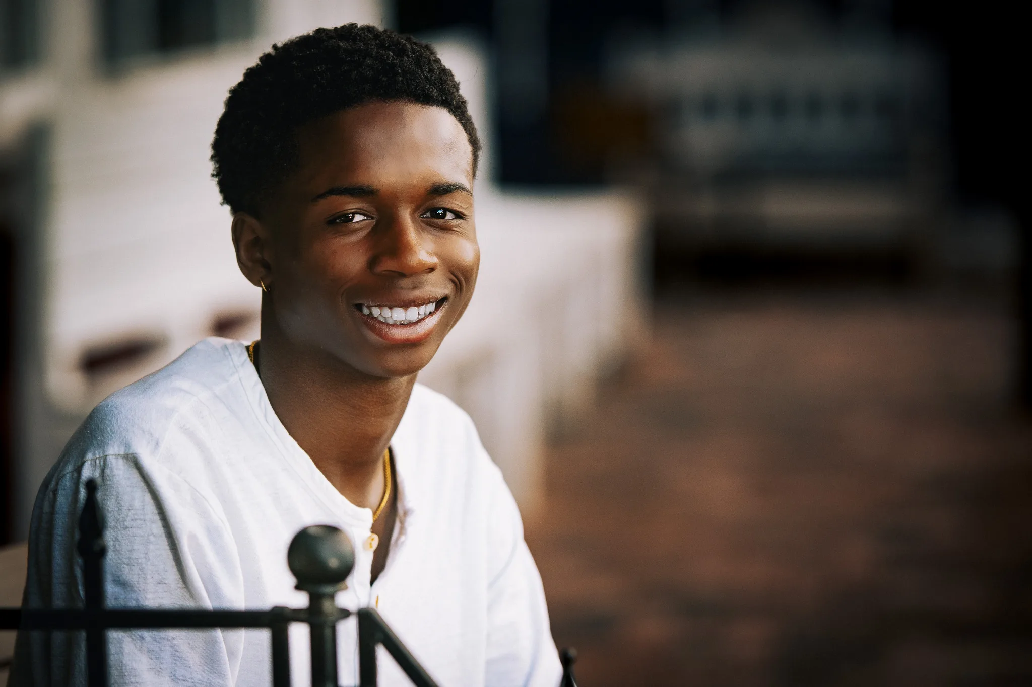Charlie smiles broadly beside an iron railing, a brick patio blurred behind him.