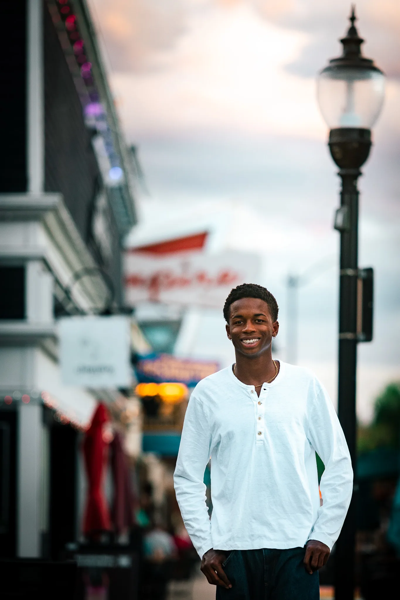 Charlie smiles on a downtown sidewalk beside a vintage lamp post under a pastel evening sky.