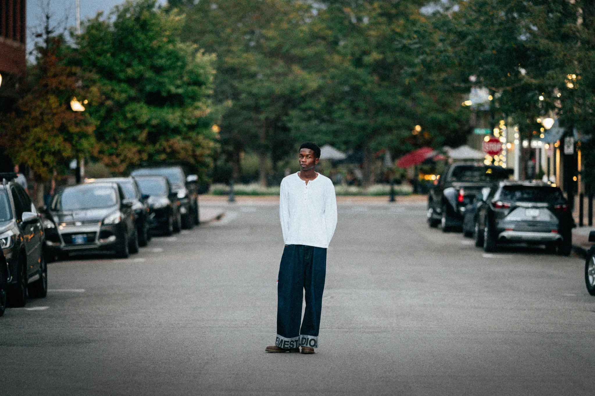Charlie stands in the middle of a quiet downtown street at dusk, parked cars on either side.