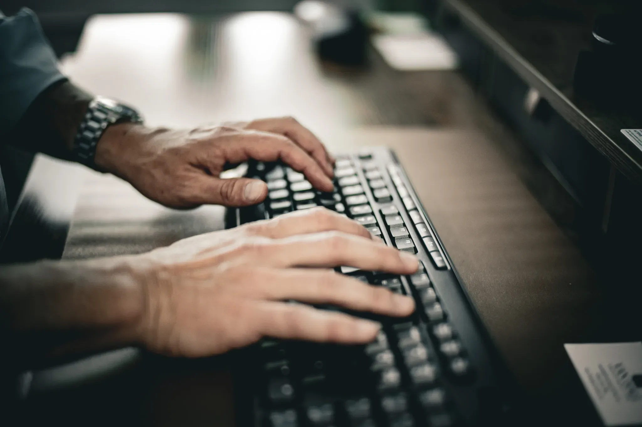 Hands typing on a black keyboard at a desk in the Wick & Trautwein office in Fort Collins, with a wristwatch visible.